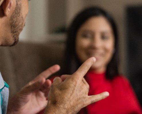 Op de afbeelding zijn twee mensen te zien, van wie de een in gebarentaal met de ander spreekt. Een gebarentolk wordt in Nederland als een voorziening gezien. De 'tolkenvoorziening' is een van de voorzieningen waarover dit onderzoek gaat.